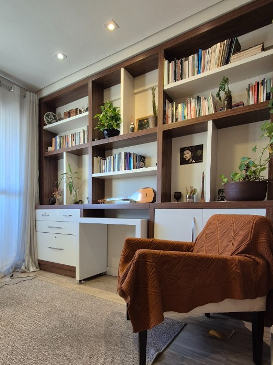Sala com biblioteca — estante de livros, mesa e poltrona